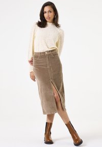 Bruine corduroy midi-rok met een zijsplit, gecombineerd met een textuurrijke crèmekleurige trui. Model draagt zwart en bruine enkellaarsjes.