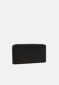 Cartera de cuero negro con una superficie texturizada, cierre tipo zip alrededor y forma rectangular. Presenta acentos en tono dorado.