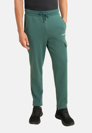 Pantalons de survêtement verts en tissu doux, avec une taille élastique et un cordon de serrage, des poches latérales et une poche cargo sur la jambe droite.