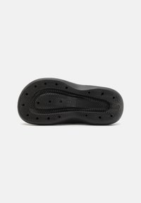 Zwarte rubberen schoenzool met een visgraatpatroon, afvoergaten en een gestructureerd oppervlak voor grip. Cirkelvormig logo gecentreerd en in reliëf aangebracht.