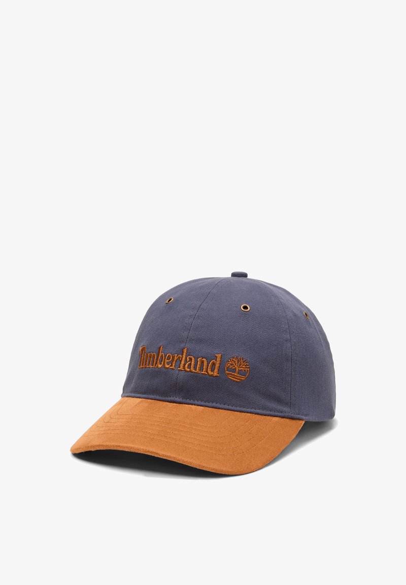 Casquette de baseball Timberland bleu marine et marron avec logo brodé et œillets de ventilation sur fond blanc.