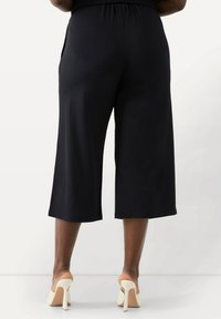 Svarta korta byxor med avslappnad passform, elastisk midja och mjukt material, tillsammans med krämfärgade högklackade sandaler.