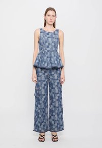Denim peplum top s vzorom štvorcov, v kombinácii s nohavicami so širokými nohavicami, ktoré majú podobný dizajn a predným cargo vreckom. Tmavomodrá farba.