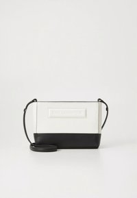 Mala pravokutna crossbody torba s bijelim gornjim i crnim donjim dijelom, s crnim remenom i utisnutim logotipom na prednjoj strani.