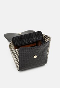 Kudottu musta ja kerma handbag, jossa on jämäkkä muoto, kultaiset metalliosat ja vetoketjullinen sisätasku, jossa on ruutukuvio.