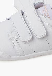 Scarpe bianche in pelle con fasce in velcro, suola testurizzata e dettagli di cucitura a contrasto. Finitura liscia con piccole perforazioni per la traspirabilità.