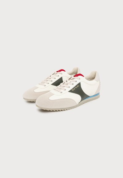 Paire de baskets basses blanches avec des accents en suède beige, des panneaux latéraux vert foncé, une doublure intérieure rouge et une bande bleue sur le bord de la semelle.
