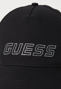 Fekete baseball sapka sima anyaggal és lekerekített koronával. A "GUESS" logó csillámló kövekkel díszíti az elülső részt.