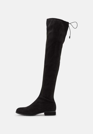 Botte plate noire au-dessus du genou avec un bout arrondi, un talon bas et un cordon ajustable en haut de la tige.