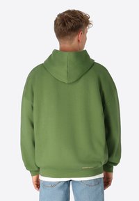Übergroßer grüner Hoodie aus Baumwollmischung, mit Kordelzugkapuze, gerippten Bündchen und einem dezenten Logo am Saum. Weiche Textur.