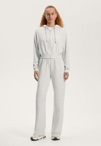 Svetlošedý športový potez s kapucňou, so zipsom na prednej strane, elastickým pásom a dlhými rukávmi. Mäkká textúra a voľný strih s ladiacimi teniskami.