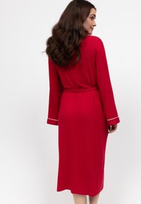 Rode lange mouwen nachtjapon met een strikceintuur, voorzien van witte biesjes op de manchetten, gemaakt van zachte stof en tot halverwege de kuit. Soepele textuur.