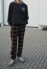 Sudadera negra con acentos grises y logotipo, combinada con pantalones de cuadros en tonos marrón y negro. Zapatillas ligeras grises con suelas texturizadas.