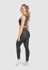 Completo da sport nera composto da reggiseno e leggings, caratterizzato da un design elegante, una texture liscia e leggings a vita alta con vestibilità aderente. Scarpe sportive bianche.