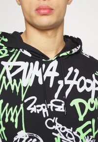 Felpa nera con testo in stile graffiti bianco e verde neon. Presenta un cordino, una texture morbida e un cappuccio regolabile.