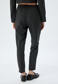 Aangepaste donkergrijze broek met een elastische tailleband, slim fit en een gladde textuur, gecombineerd met glanzende zwarte loafers.