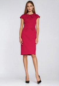 Dopasowana magentowa sukienka z krótkimi rękawami typu czapka, plisowanym dekoltem i podkreśleniem talii, o długości do kolan, w zestawieniu z czarnymi butami na wysokim obcasie.