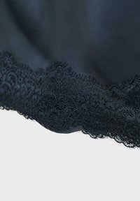 Czarna tkanina z misterną koronkową aplikacją kwiatową z ząbkowanymi brzegami na elemencie ubrania lub tkaniny.