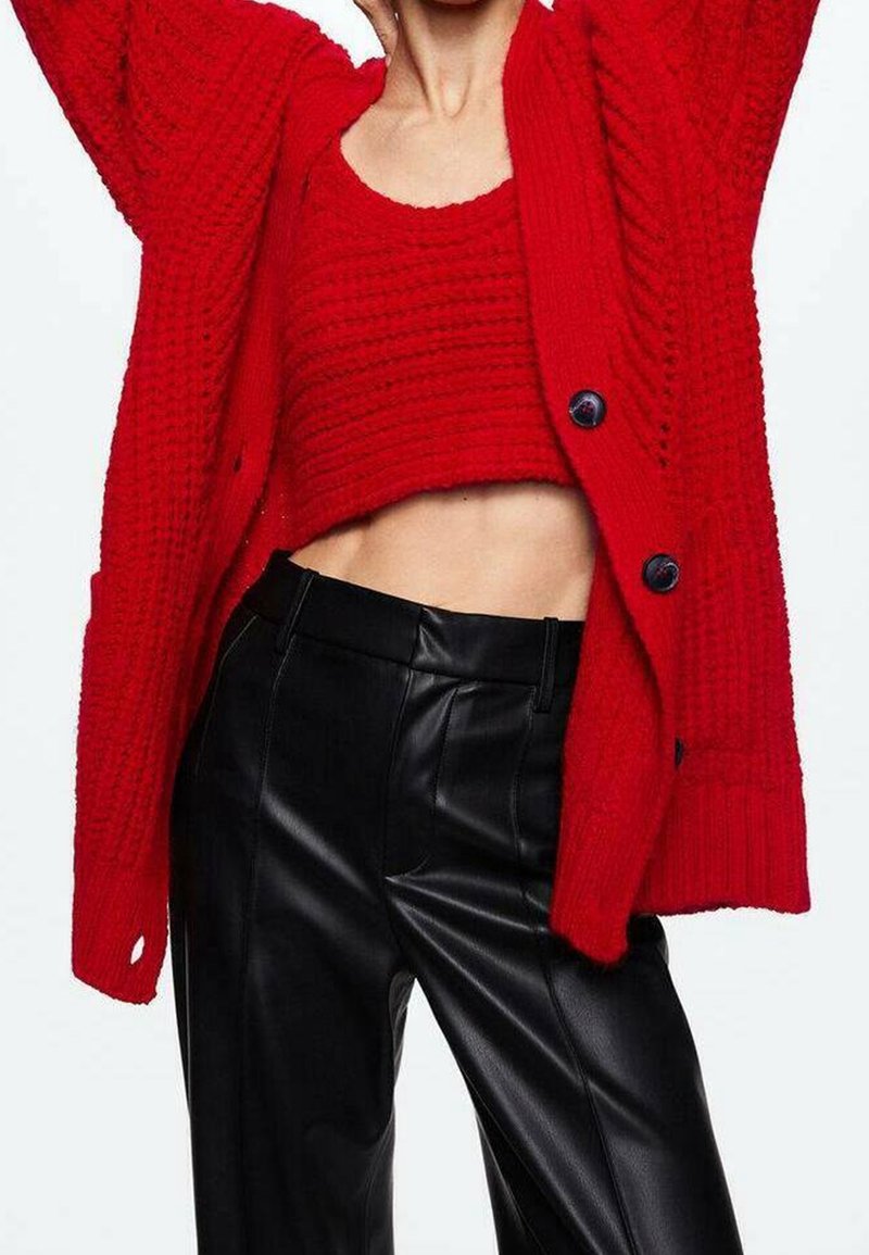Punainen neulecardigan, jossa on paksu rakenne ja suuria nappeja, kerrostettuna vastaavan värisen lyhyen topin päälle; yhdistettynä korkeavyötäröisiin mustiin nahkahousuihin.