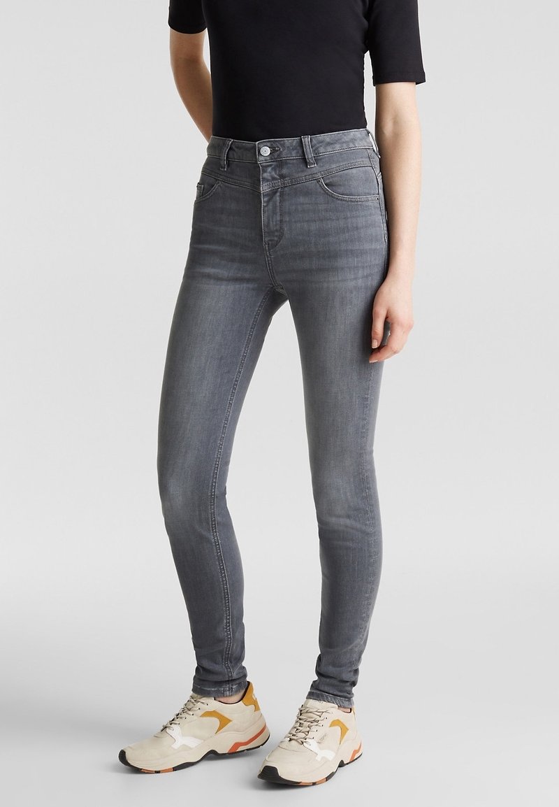 Smala jeans i grå denim, hög midja med framfickor, subtila slitningar, kombinerat med beige sneakers.