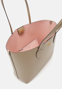 Lys grå tote-veske med brune håndtak og rosa innside. Har en glidelåslomme inni og trykknapplukking. Glatt tekstur, minimalistisk design.