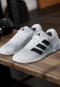 Λευκά αθλητικά παπούτσια με υφασμένη επάνω επιφάνεια, τρεις μαύρες ρίγες, ενισχυμένη μύτη και λαστιχένια σόλα.