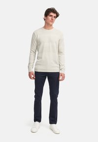 Hellgrau strukturierter Pullover mit einem runden Halsausschnitt, kombiniert mit dunkelblauen schmal geschnittenen Hosen und weißen Sneakern. Einfaches, lässiges Design.