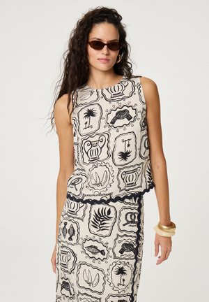 Vrouw die een mouwloos topje en rok draagt met zwarte contourpatronen van vissen, planten en vazen, geaccentueerd met een zonnebril en armbanden.