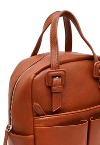 Sac à dos en cuir marron avec une surface texturée, deux poignées supérieures, une fermeture éclair et des poches avant pour le rangement.