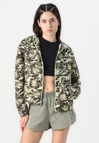 Floral zip-up jacket in green and brown, featuring a cropped cut, long sleeves, and a black crew neck t-shirt with olive shorts.