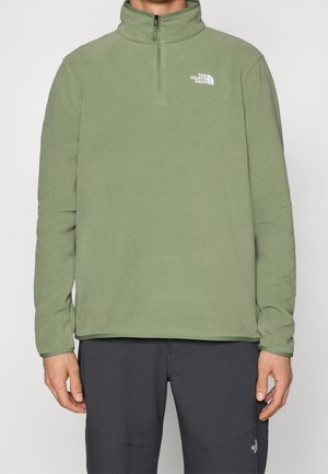 Pull-over en polaire verte avec col montant et demi-fermeture éclair, arborant un logo blanc sur la poitrine. Texture lisse et coupe décontractée.