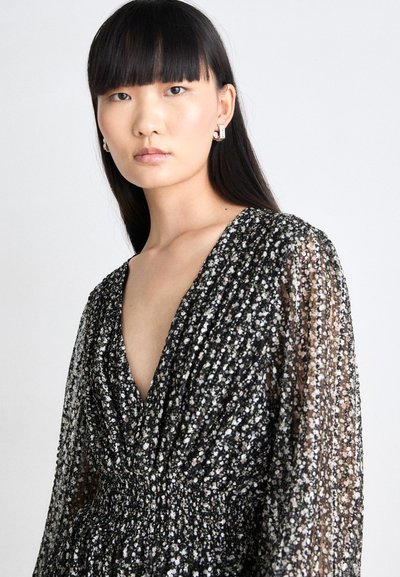Schwarzes Kleid mit durchsichtigen langen Ärmeln, das über einen tiefen V-Ausschnitt und Raffung in der Taille verfügt. Verz decoration, welch verstreuten Blumen-Mustern in Weiß und Blush.