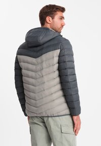 Vuorattu takki hupulla, jossa on harmaa ja tummanharmaa viivakuvio, tikattu pinta ja etuvetoketju.