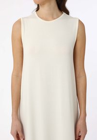 Bezramínkov dresses ve smetanové barvě, měkká tkanina, uvolněný střih, kulatý výstřih, lem sahající pod kolena, minimalistický design bez vzorů nebo ozdob.
