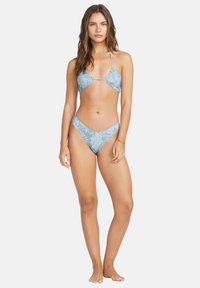 Modrý vzorovaný bikiny s trojuholníkovým vrchom a nízko vyrezanými spodkami. Materiál vyzerá hladko; má tenké popruhy a minimálne pokrytie.
