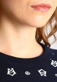 Marinblått stickat tröja med ribbad halsringning och vita mönstrade detaljer, inklusive symboler och former i hela tyget.