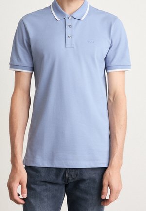 Homme portant un polo bleu clair à manches courtes avec bordure blanche au col et aux manches, associé à un jean bleu foncé.