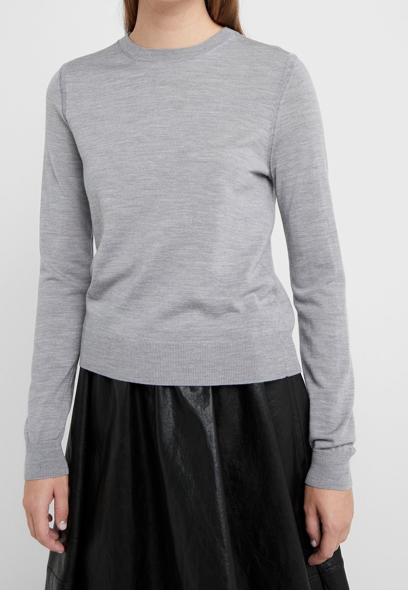 Šedý dlouhý svetr s dlouhými rukávy vyrobený z měkké pleteniny, s kulatým výstřihem a žebrovanými manžetami, kombinovaný s černou koženou sukní.