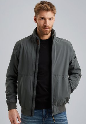 Giacca bomber grigia scura con colletto alto, zip frontale e polsini a costine. Realizzata in materiale liscio, presenta tasche laterali e cuciture sottili.