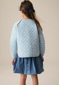 Giacca blu trapuntata con motivo floreale, design imbottito e orlo arrotondato, abbinata a una gonna di jeans con pieghe e forma svasata.
