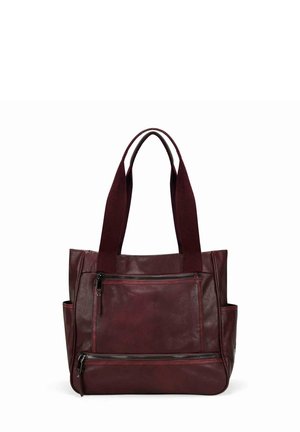 Sac cabas en cuir rouge foncé avec deux longues anses, poche zippée à l'avant, compartiment zippé inférieur et poches latérales ouvertes.