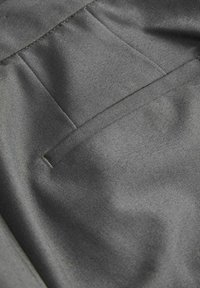 Grijze stofclose-up met een gladde textuur, diagonale naden en een zakdetail, dat een gestructureerde maar toch zachte uitstraling benadrukt.