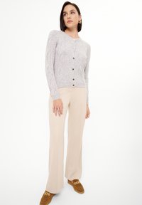 Cardigan grigio chiaro a maglia testurizzata con bottoni frontali, abbinato a pantaloni beige a gamba larga e mocassini in suede marrone.