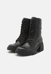 Botas de cuero negras hasta el tobillo con un diseño robusto, que cuentan con cordones prominentes, un tiro ligeramente acolchado y un tacón grueso para mayor estabilidad.