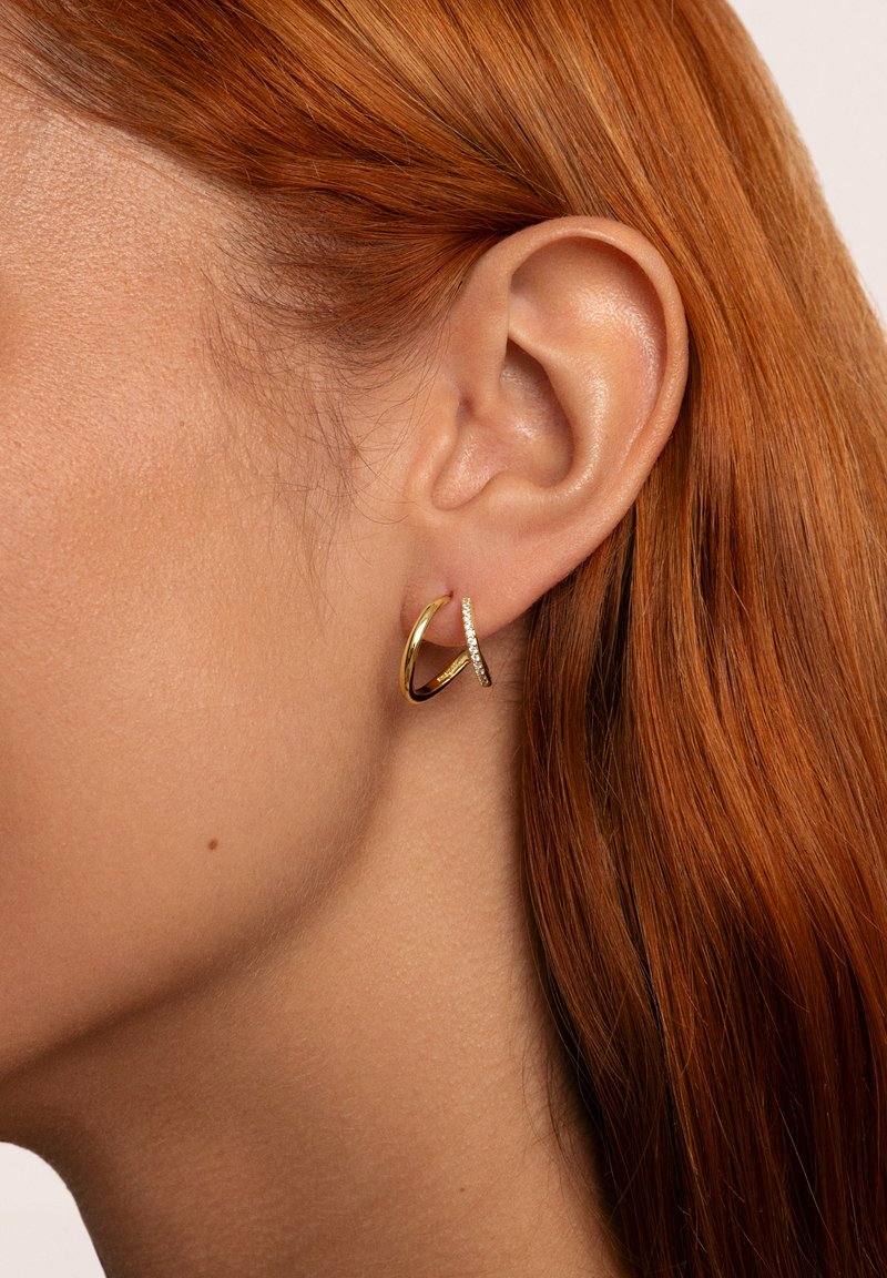 Goldene Creolen mit polierter Oberfläche, die ein schlankes, strukturiertes Akzentdetail aufweisen. Das Design ist minimalistisch mit eleganten Kurven.