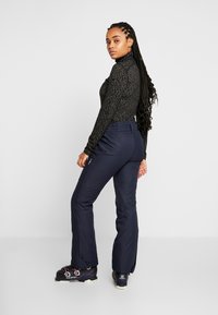 Sort langærmet top med sølv abstrakt mønster, parret med marineblå bukser og sorte skistøvler med pink accenter og stropper.