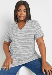 Randig kortärmad polo t-shirt med v-ringning i svart och vitt, tillverkad av mjukt tyg. Bärs med blå jeans.