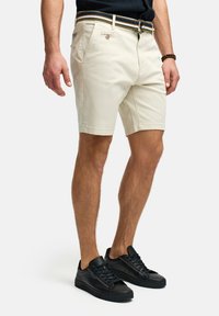 Beige katoenen shorts met riemlussen, voorzakken en een knoopsluiting. Gecombineerd met zwarte leren sneakers voor een casual look.