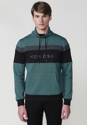 Sudadera verde con cuello alto, con rayas horizontales en negro y gris, un bolsillo frontal y el texto "KORÖSHI" en el pecho.