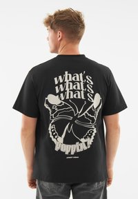 Černé bavlněné tričko s velkým bílým potiskem motýla a textem na zadní straně. Krátké rukávy a standardní střih.